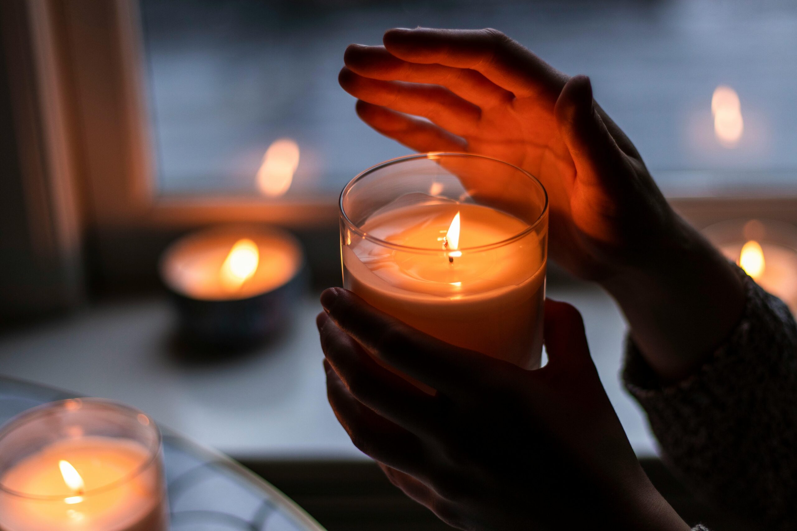 Mano che tiene una candela accesa, che crea una luce soffusa, nello sfondo ci sono altre candele