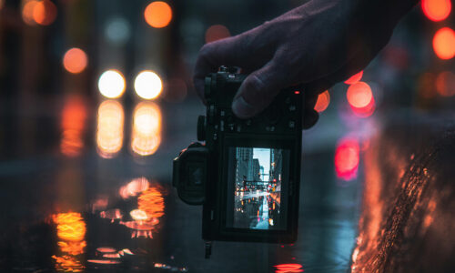 Ragazzo con fotocamera mirrorless Sony Alpha che scatta una foto di strada notturna