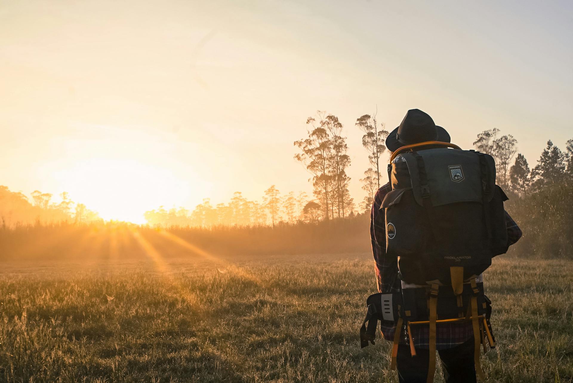 Uomo con cappello e con uno zaino da viaggio cammina verso un tramonto