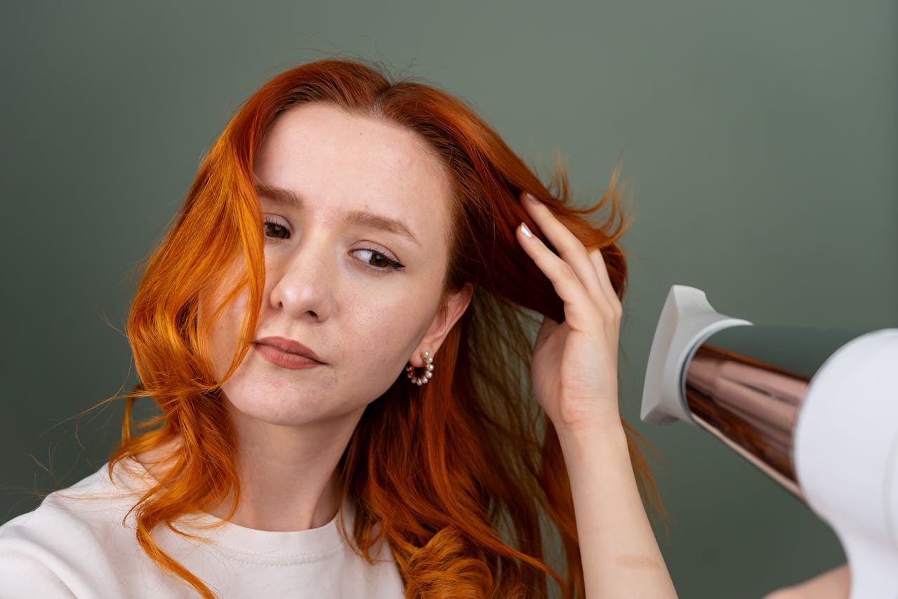 Donna con capelli rossi che utilizza un asciugacapelli per modellare i capelli davanti a uno specchio