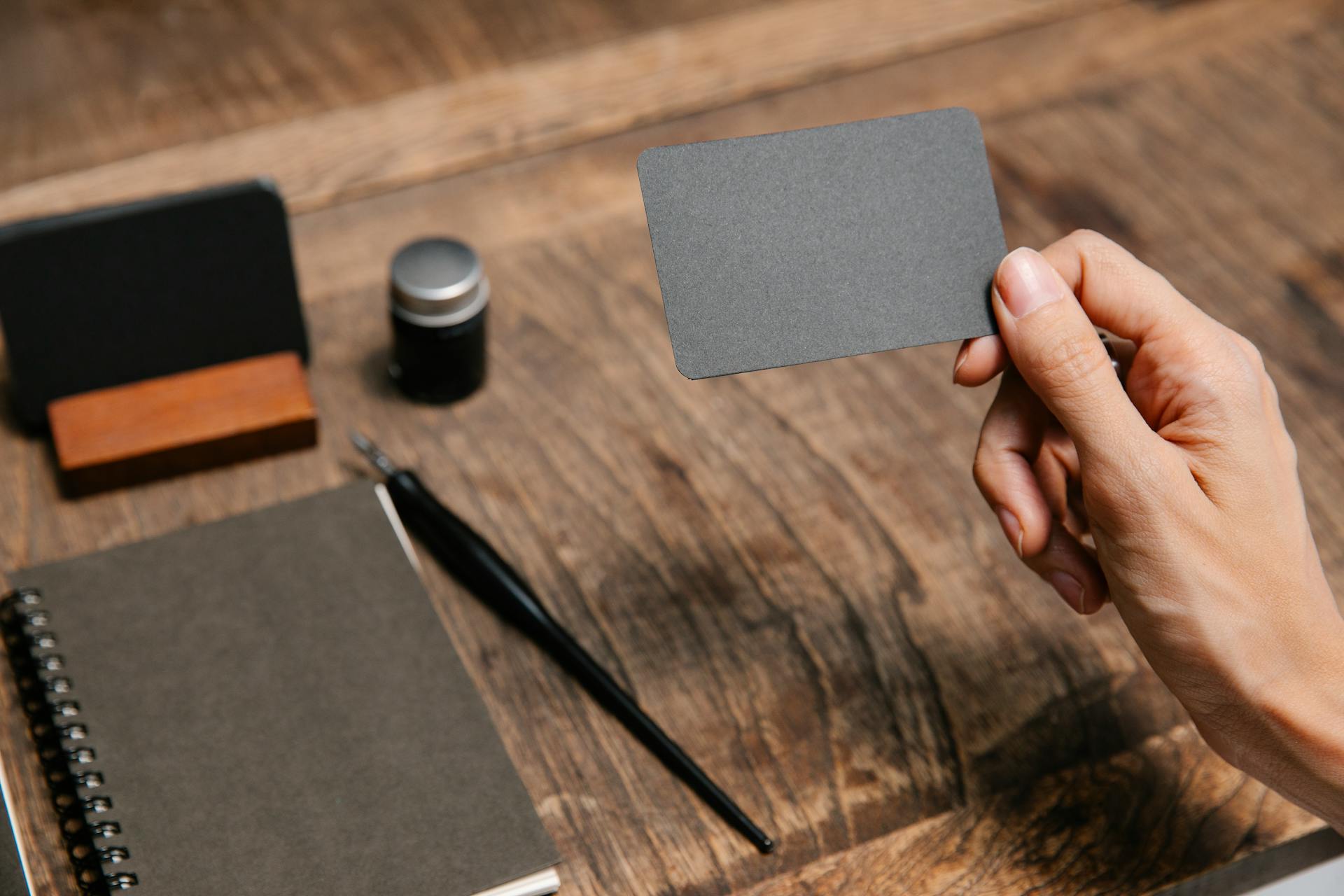 Mockup di biglietto da visita nero minimalista tenuto in mano su scrivania in legno