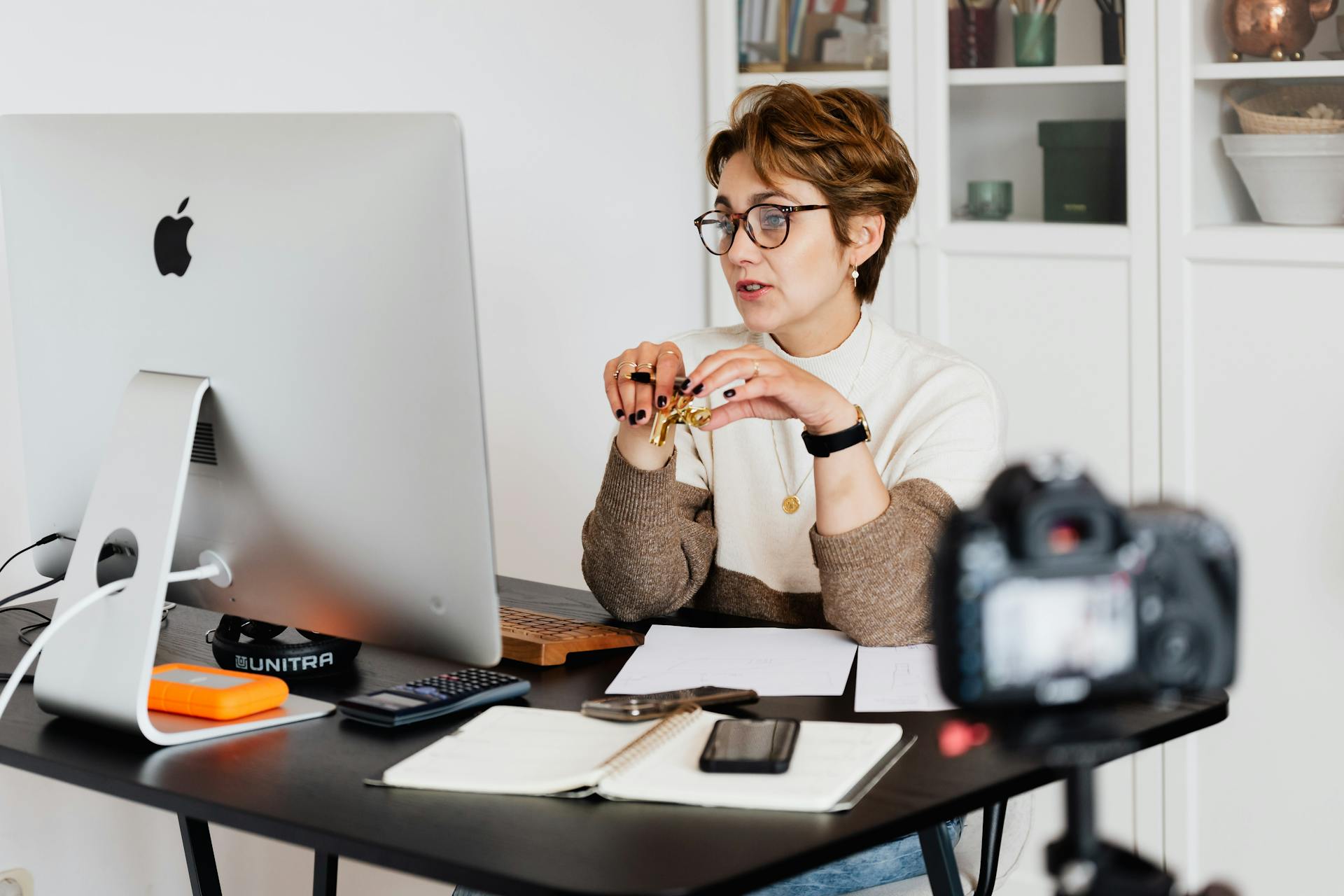 Donna al lavoro su computer Apple con fotocamera su scrivania per produzione contenuti digitali