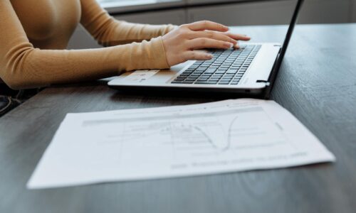 Persona al computer in ambiente professionale con documenti cartacei per analisi dati e formazione aziendale