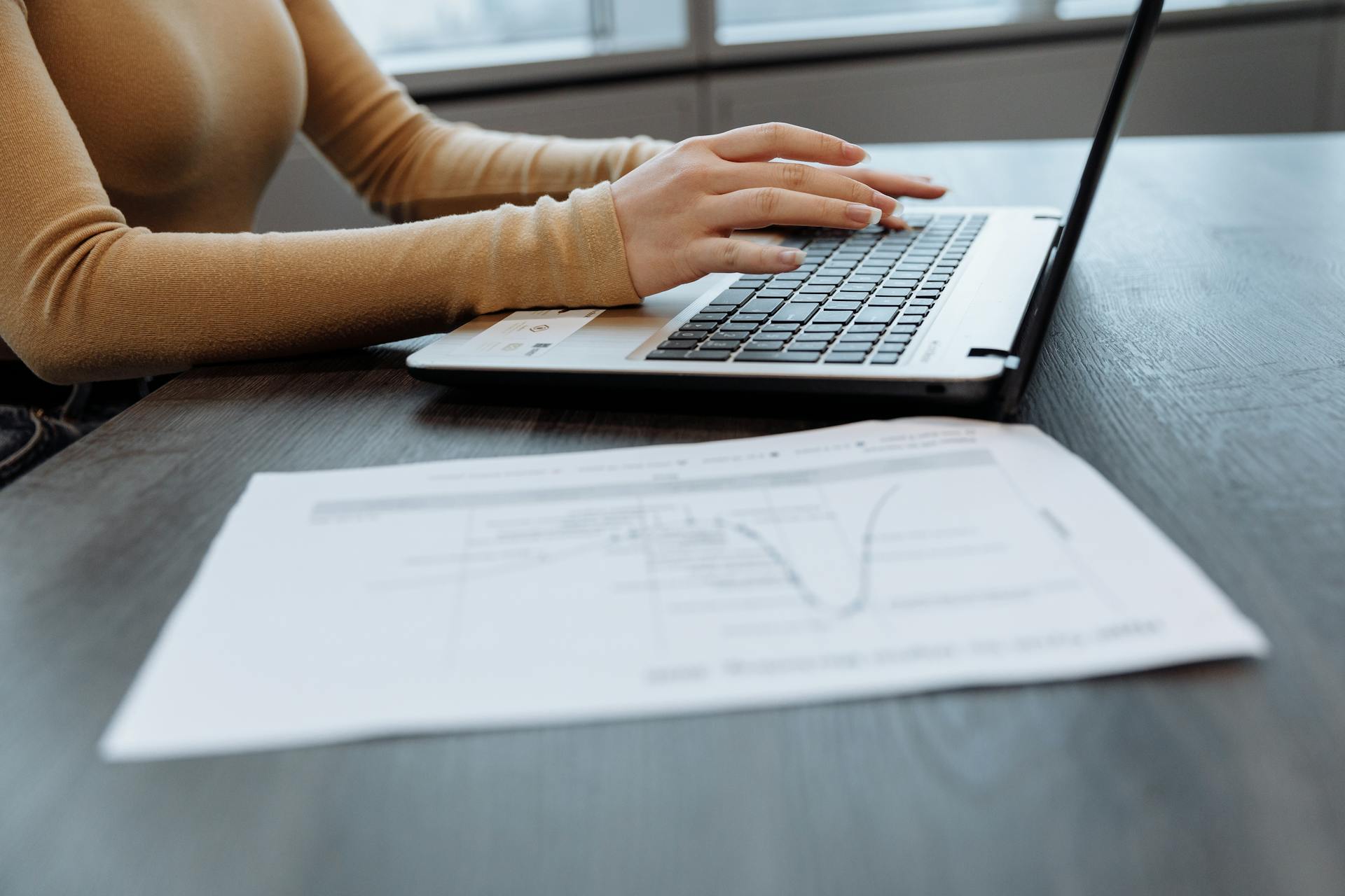 Persona al computer in ambiente professionale con documenti cartacei per analisi dati e formazione aziendale