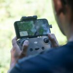 Pilota di drone che controlla un dispositivo DJI con smartphone durante un volo aereo