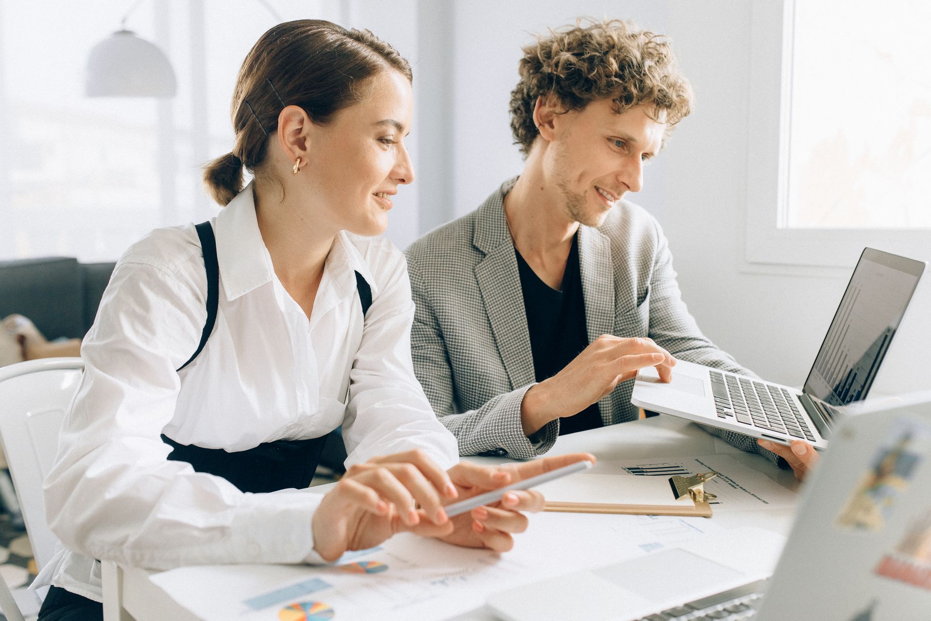 Due colleghi in ufficio collaborano analizzando grafici finanziari su un computer portatile e condividendo dati da uno smartphone