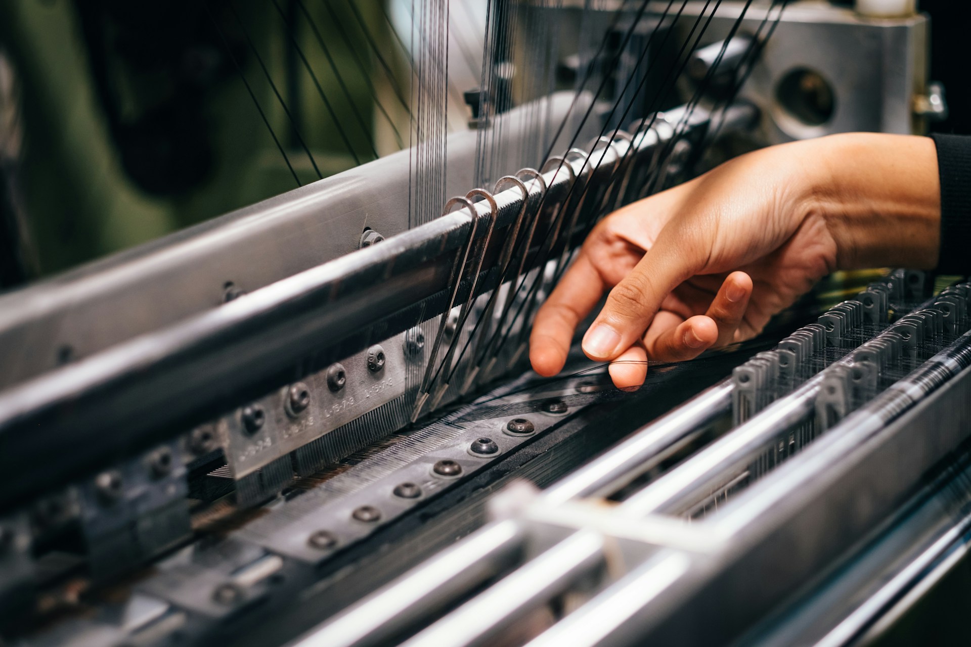 Primo piano delle mani di un artigiano che lavora ai filati su un telaio meccanico in un'industria tessile.