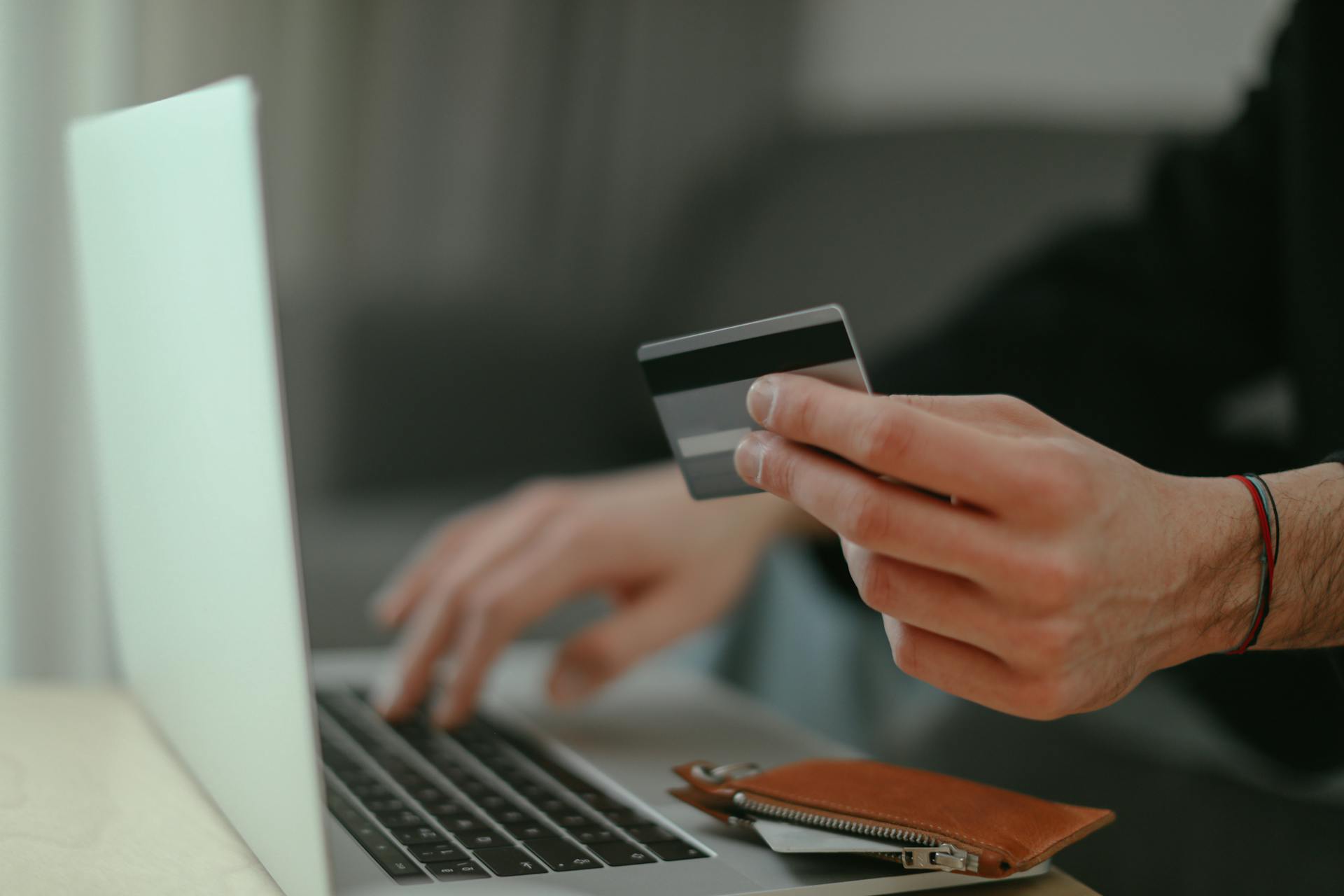 Persona che digita sulla tastiera di un computer portatile mentre tiene in mano una carta di credito per un acquisto online
