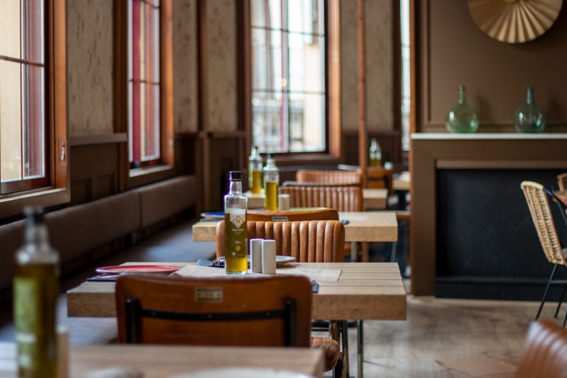 Tavoli in legno apparecchiati all'interno di un ristorante moderno con bottiglia di olio d'oliva in primo piano.